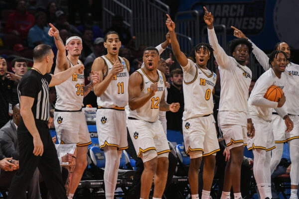 The Missouri Tigers Basketball team bench points in the opposite direction to which a referee is pointing during a March Madness First Round college basketball game.